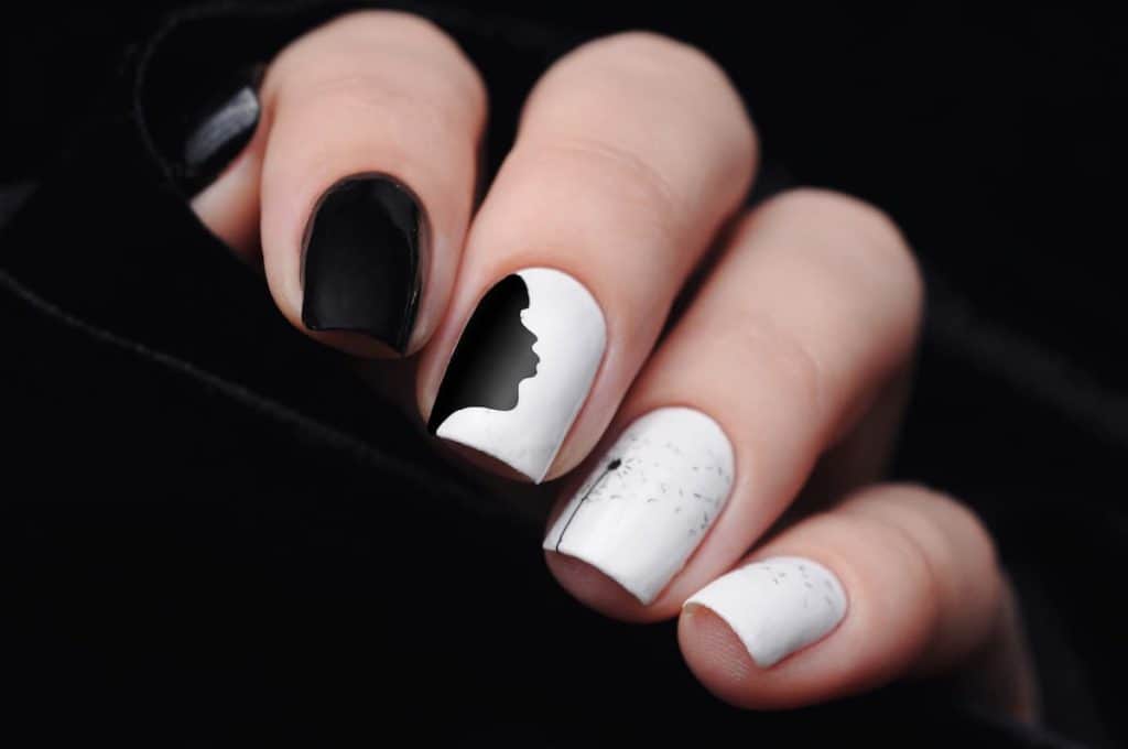 A woman's hands that has a combination of black and white nail polish with a silhouette of a girl nail design