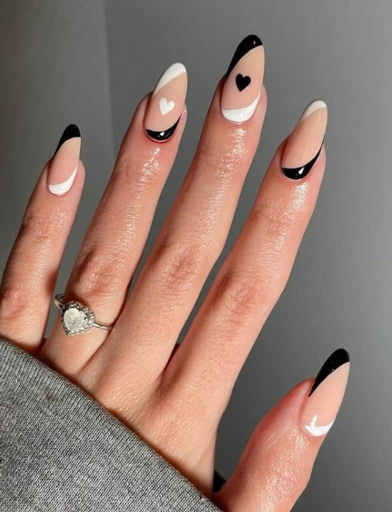 A woman's hands with a combination of nude, black and white nail polish. It has little black and white heart designs.