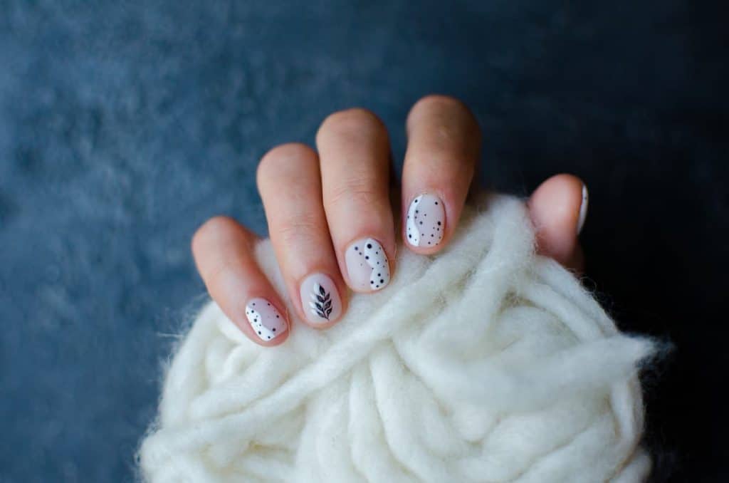 A woman's hand with beautiful white nail polish that has a combination of translucent and white base topped with black dots