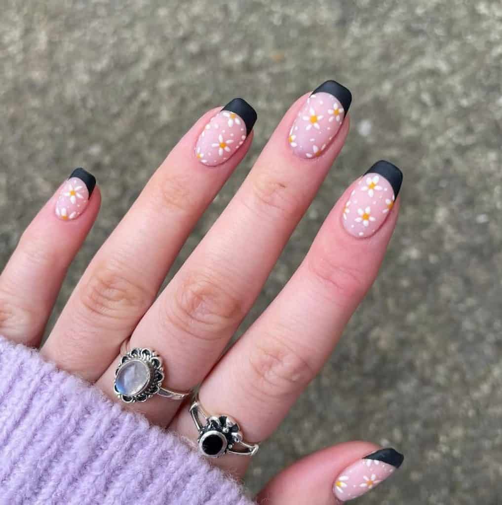 A woman's beautiful hands wearing two rings with black french tips that has white daisies design