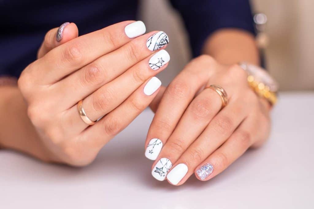 A woman's hands with beautiful white nail polish that has black stars nail design and glittery silver polish