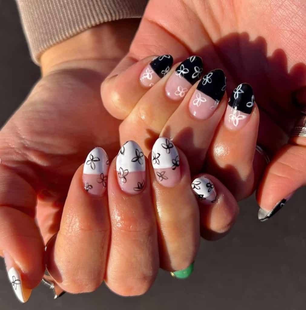 A woman's hands with nails are half-painted with white on one hand and black on the other and has lovely flowers design
