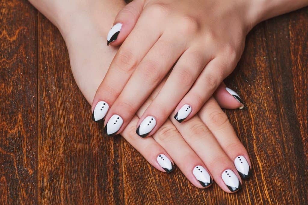 A woman's hands on top of a table with beautiful white nail polish that has a black nail tips and nail art inspired by tuxedos
