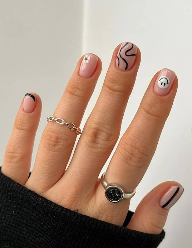A woman's hand wearing rings with a nude nail polish that has beautiful black and white nail designs