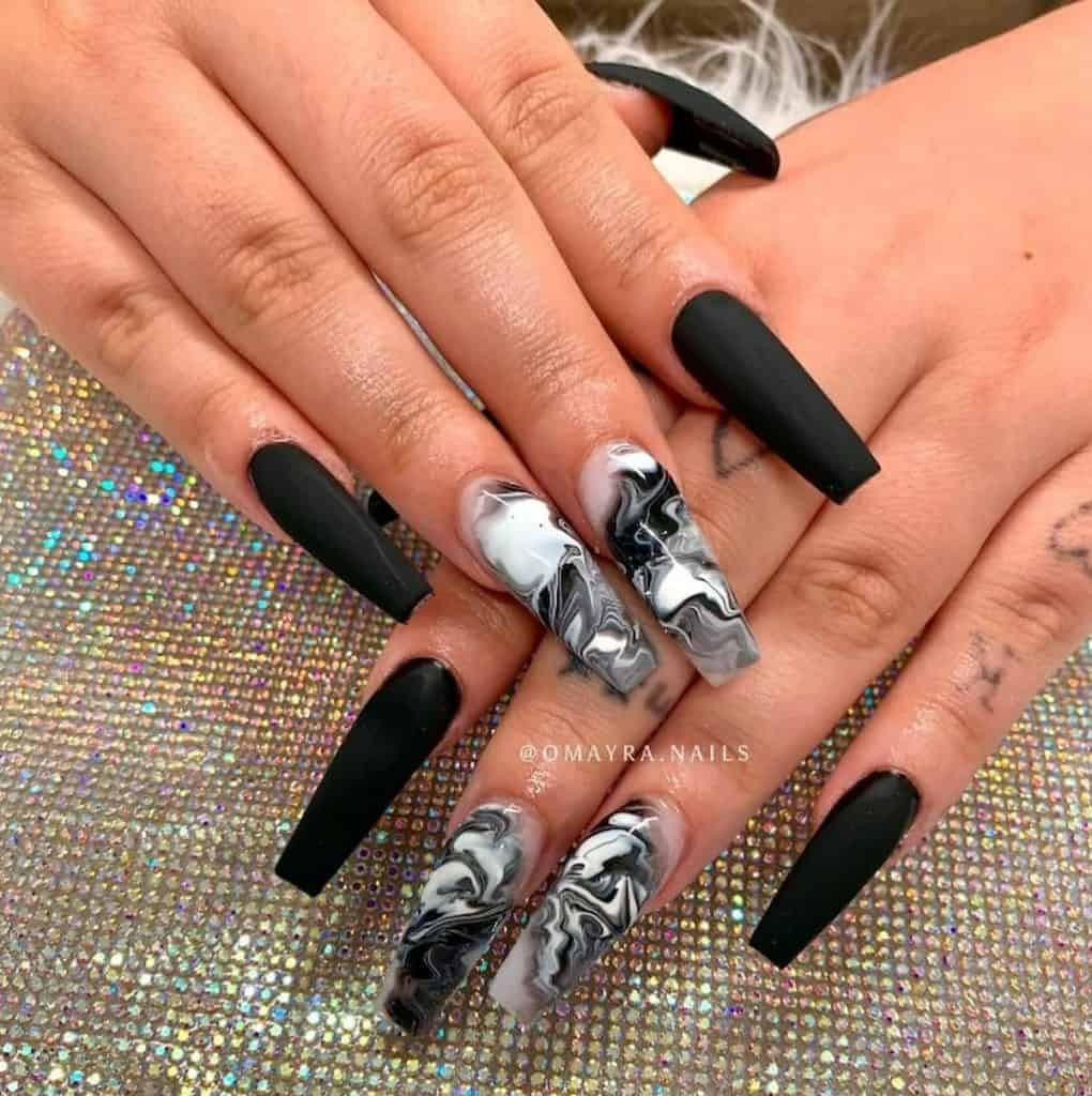A woman's hands with a matte black nail polish that has marble nails as accent 