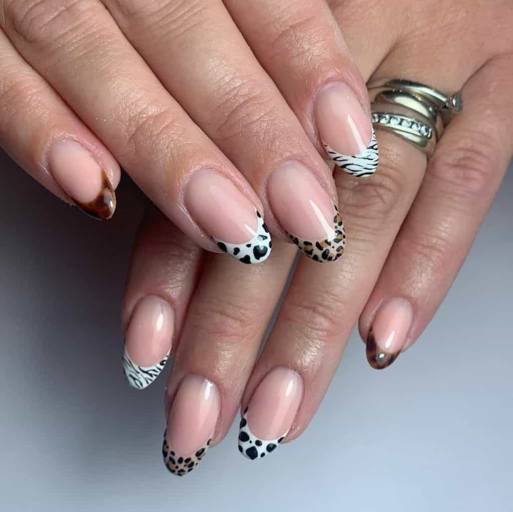 A closeup of a woman's hands with a pinkish nude nail polish that has a black and white cow prints and tiger stripes with brown giraffe and leopard spots nail tips design