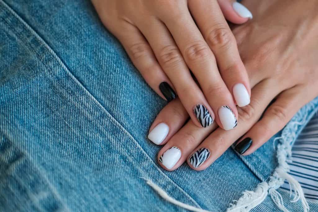 A woman's hands with a combination of beautiful white and black nail polish that has tiger print accent nails 