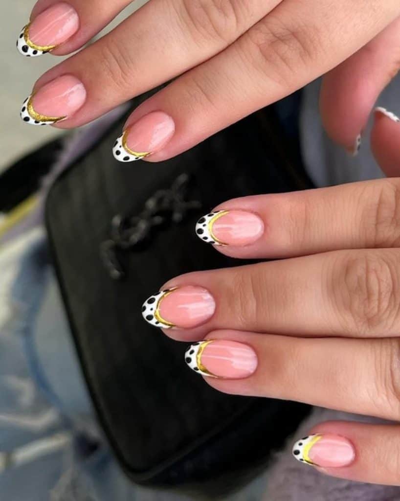 A woman's hands with a beautiful nude nail polish that has dalmatian spots nail design on the tips and gold glitter
