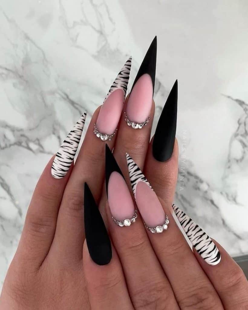 A woman's hands with a stiletto nails that has a baby pink nail base color with black and white tiger print nail design and crystals on the accent nails 