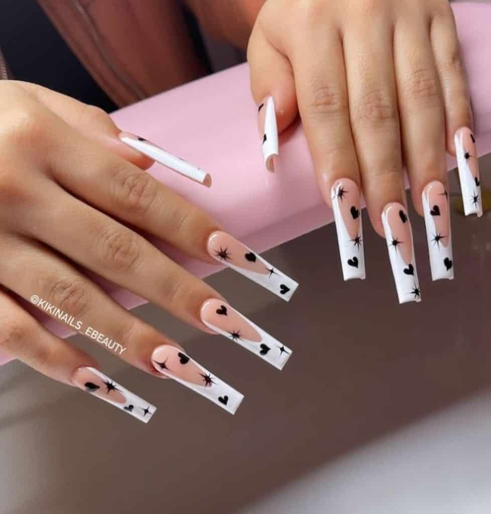 A woman's hand with a nude nail polish that has white nail tips and black hearts and sparkles nail designs