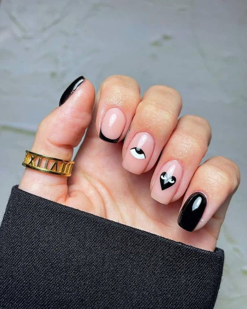 A closeup of a woman's hand with a nude and black nail polish that has a black and white eye and heart nail designs