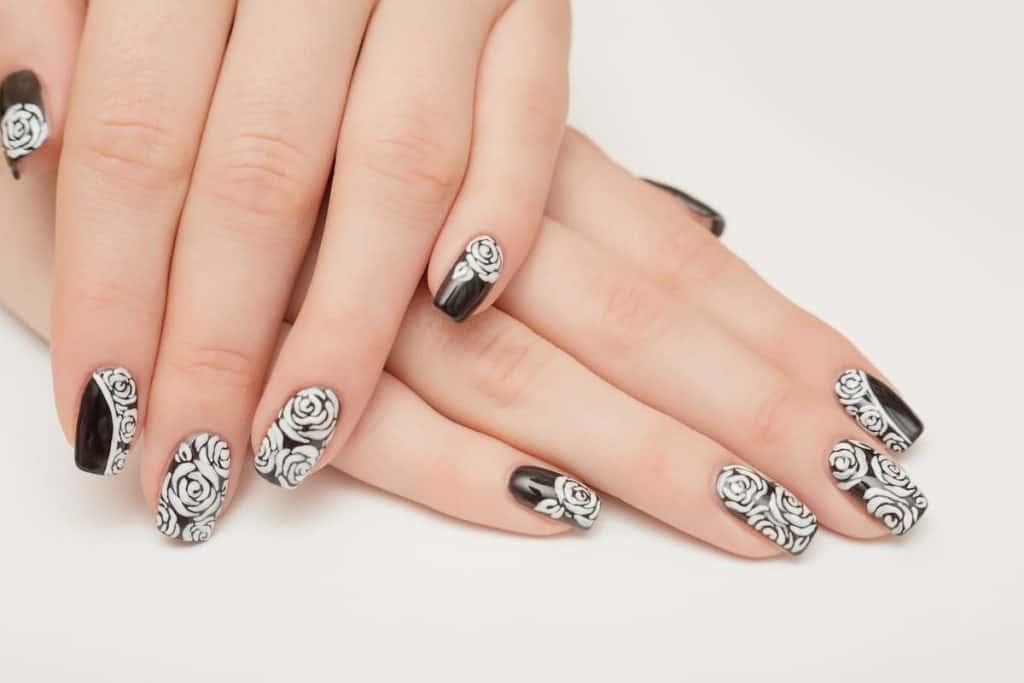 A closeup of a woman's hands with a combination of black and white nail polish that has white roses nail designs 
