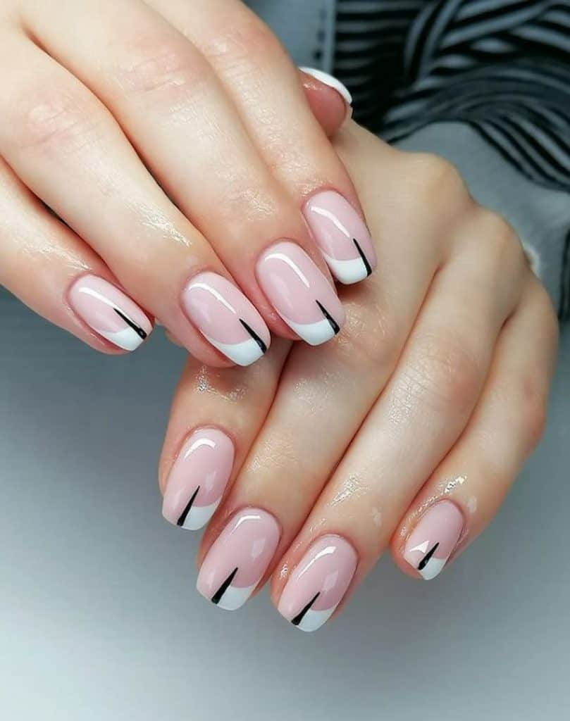 A woman's beautiful hands with a nude nail polish and white colored tips that has sharp black line in the middle of the nails