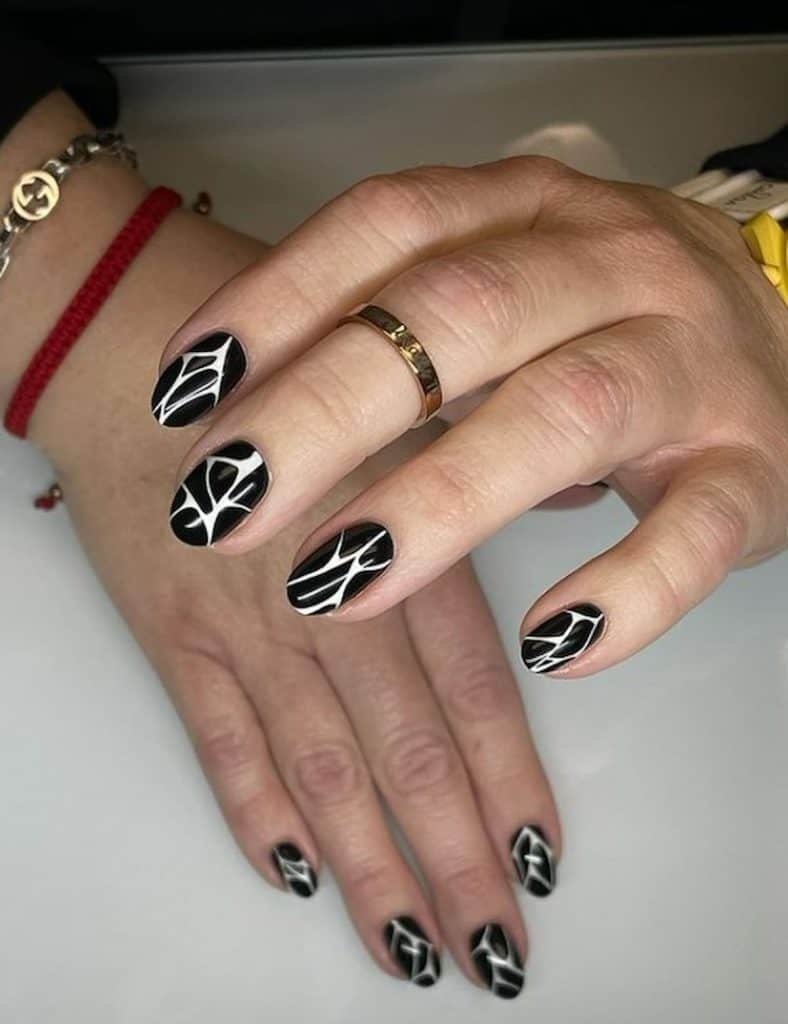 A closeup of a woman's hands with a beautiful black nail polish that has a white crack nail designs