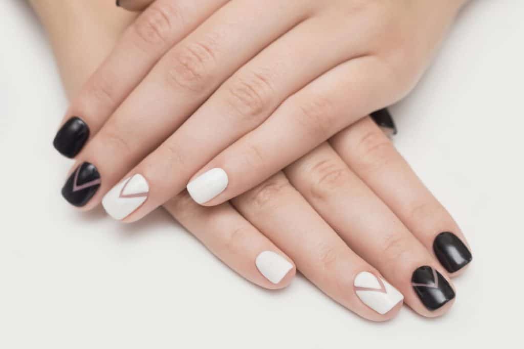 A woman's hands with a combination of black and white nail polish that has a chevron pattern nail designs
