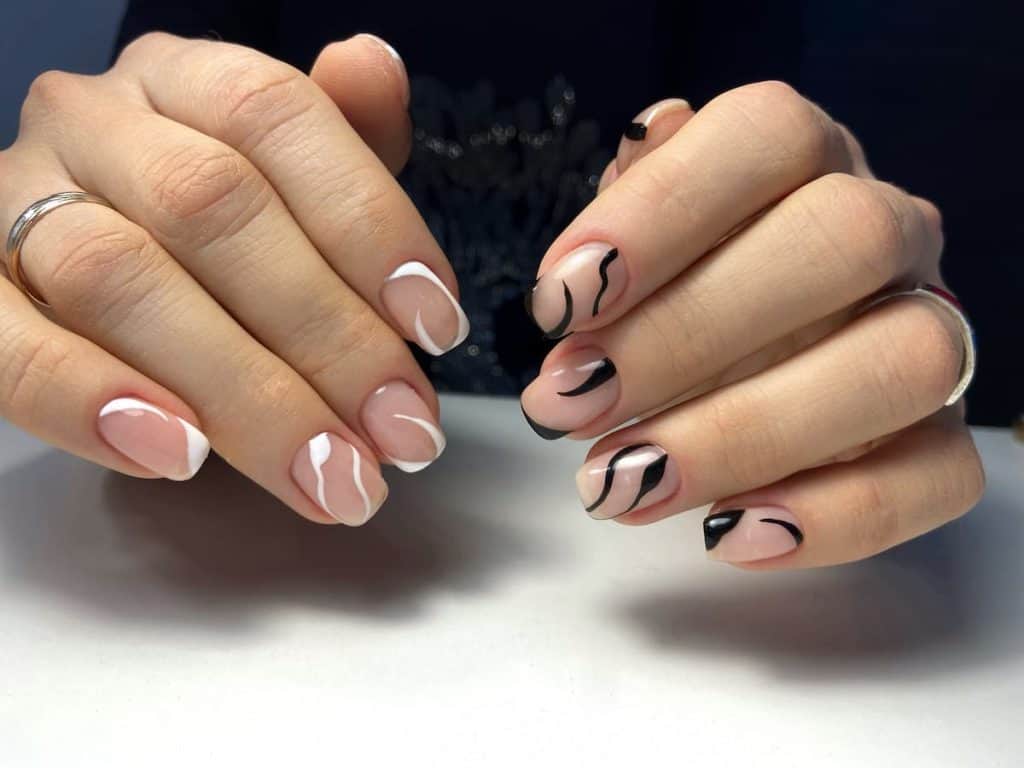 A woman's hands with a beautiful nude nail polish that has black and white swirls in different directions nail designs