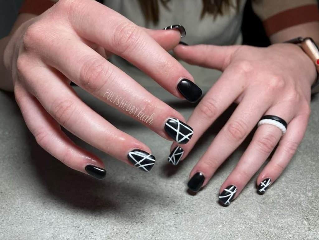 A woman's hands with black nail polish that has intersecting white lines nail designs 