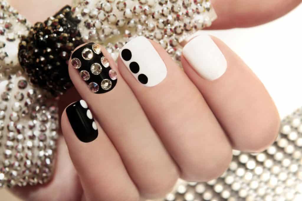 A woman's beautiful hands that has black and white nails with diamonds as polka dots on the accent nails 