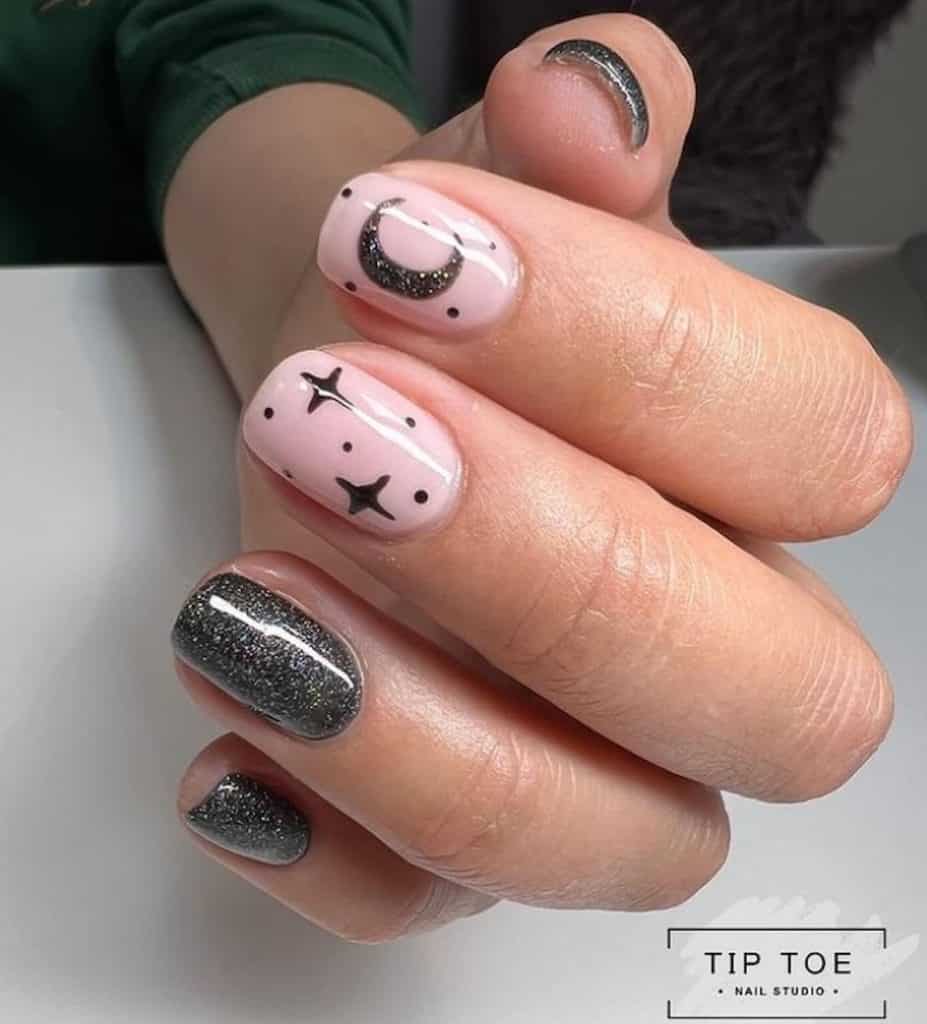 A closeup of a woman's hand with a combination of pink and black nail polish base that has glitters, dots, stars, and the moon nail designs