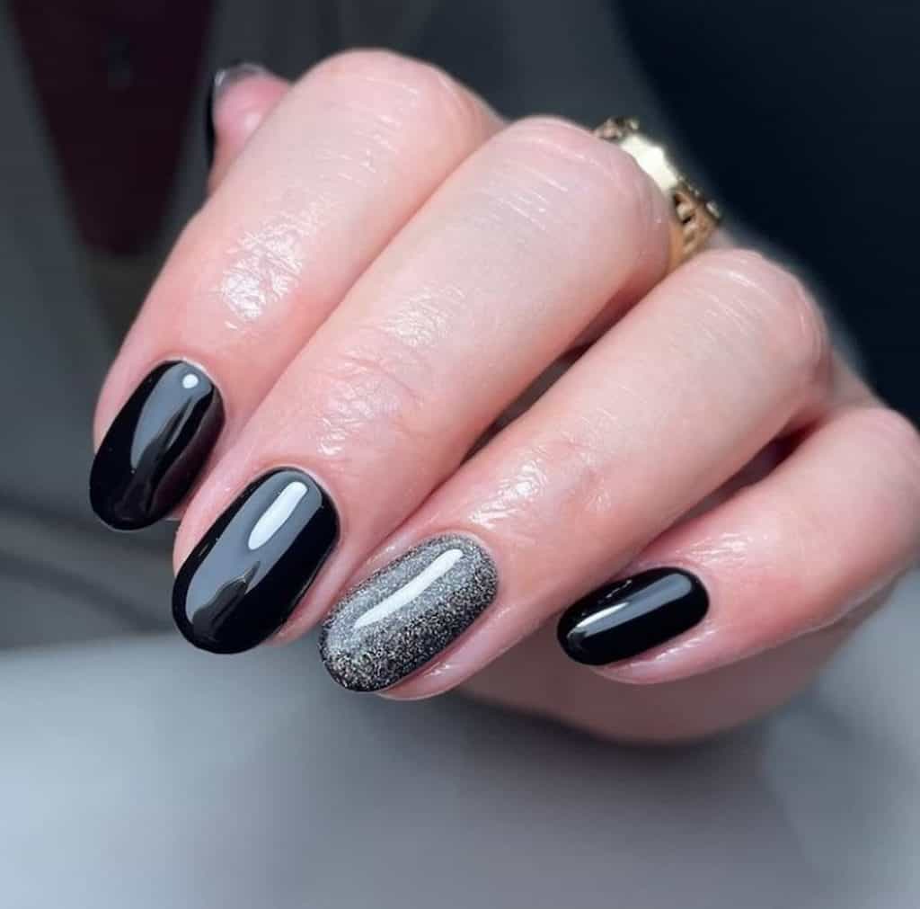 A closeup of a woman's hand with a black nail polish that has white glitter on select nails