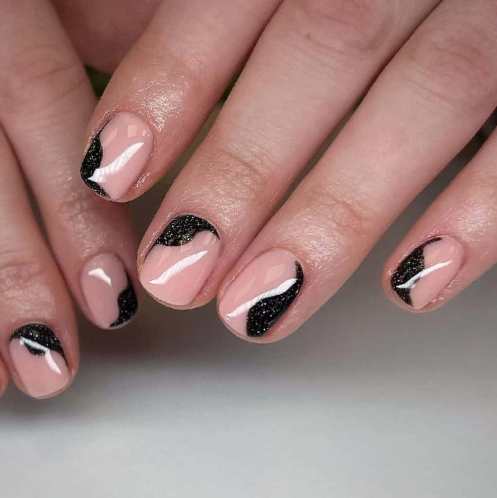 A closeup of a woman's hands with a combination of nude and black nail polish that has glitter 