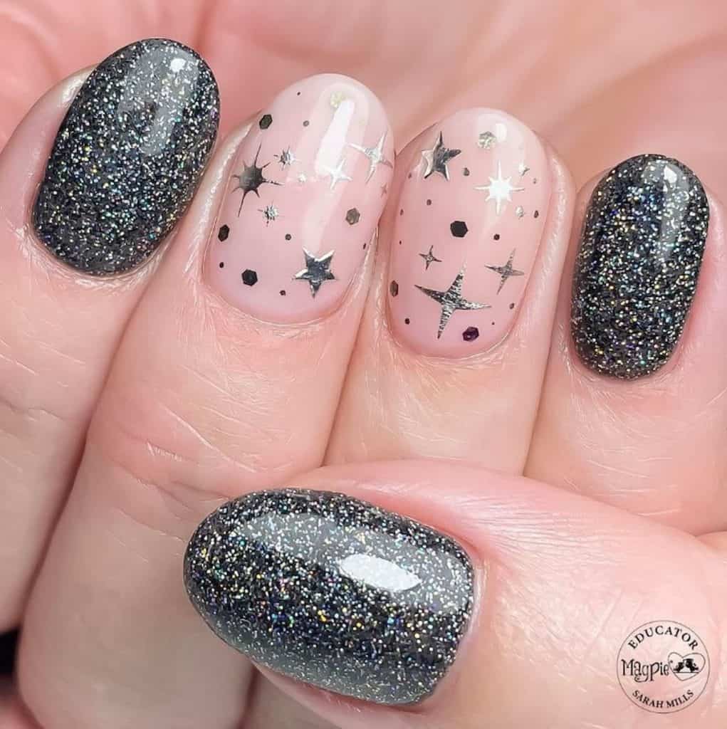 A closeup of a woman's hand with a combination of light pink and black nail polish that has glitter and silver stars nail designs on select nails