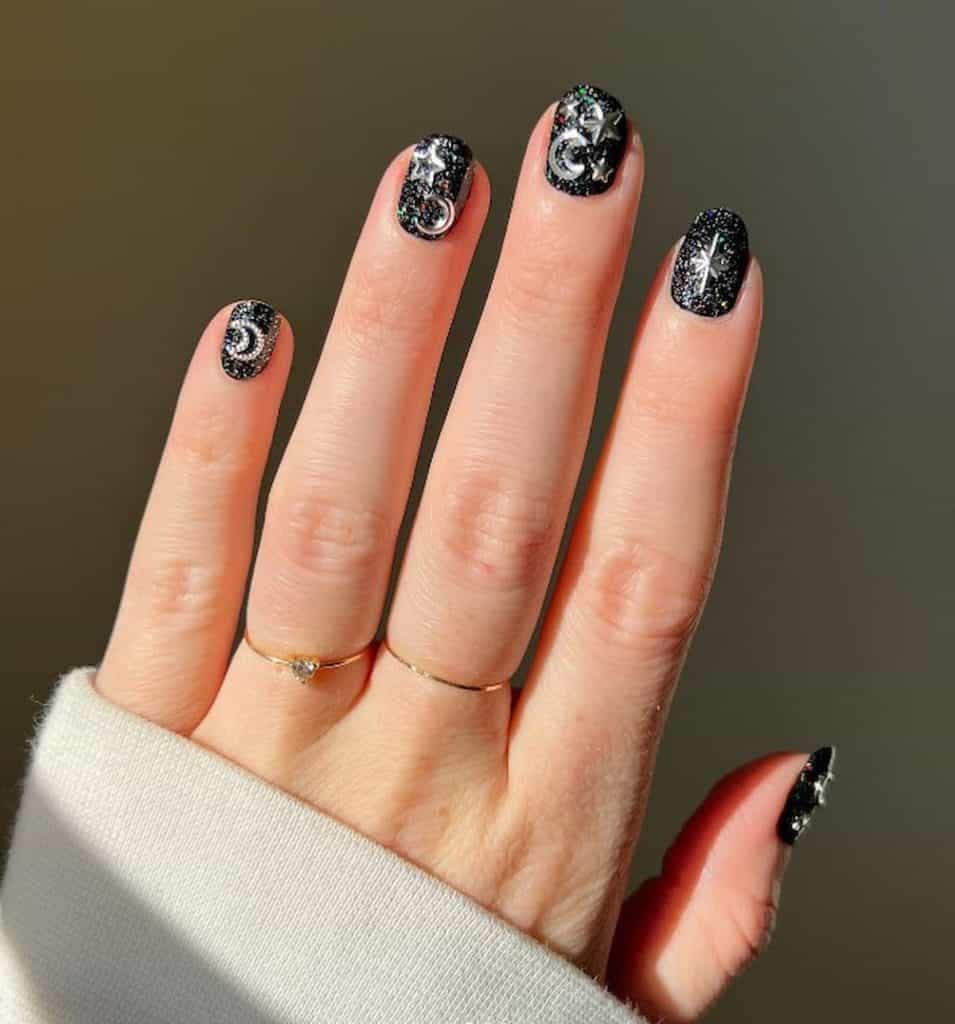 A closeup of a woman's hand with a black nail polish that has layers of silver and holographic glitter, stars and moons