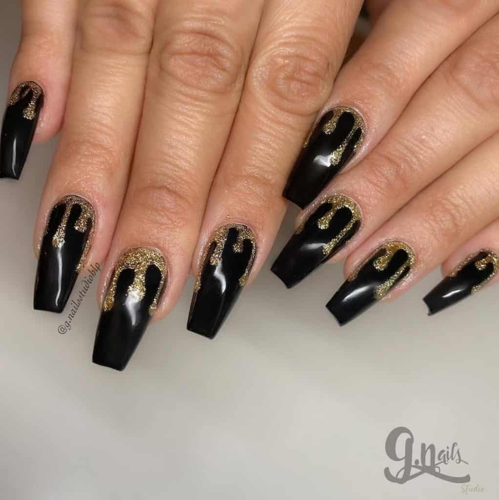 A woman's hands with black nail polish base that has gold glitter in a dripping design