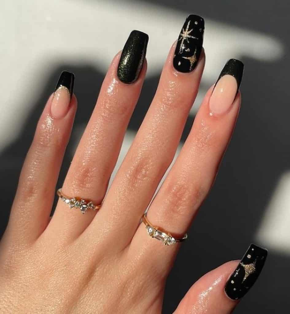 A closeup of a woman's nude and black nail polish that has golden starry accent nail and glitter