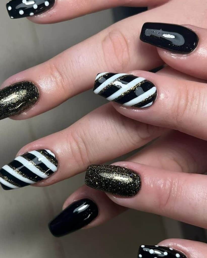 A closeup of a woman's hands with black nail polish that has white stripes, dots, and silver or gold glitter