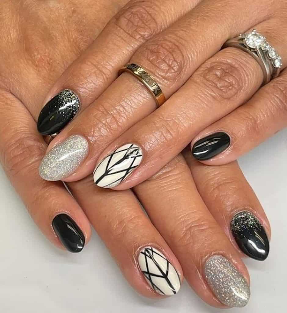 A closeup of a woman's hands with a combination of white and black nail polish that has silver shimmer and black lines on select nails