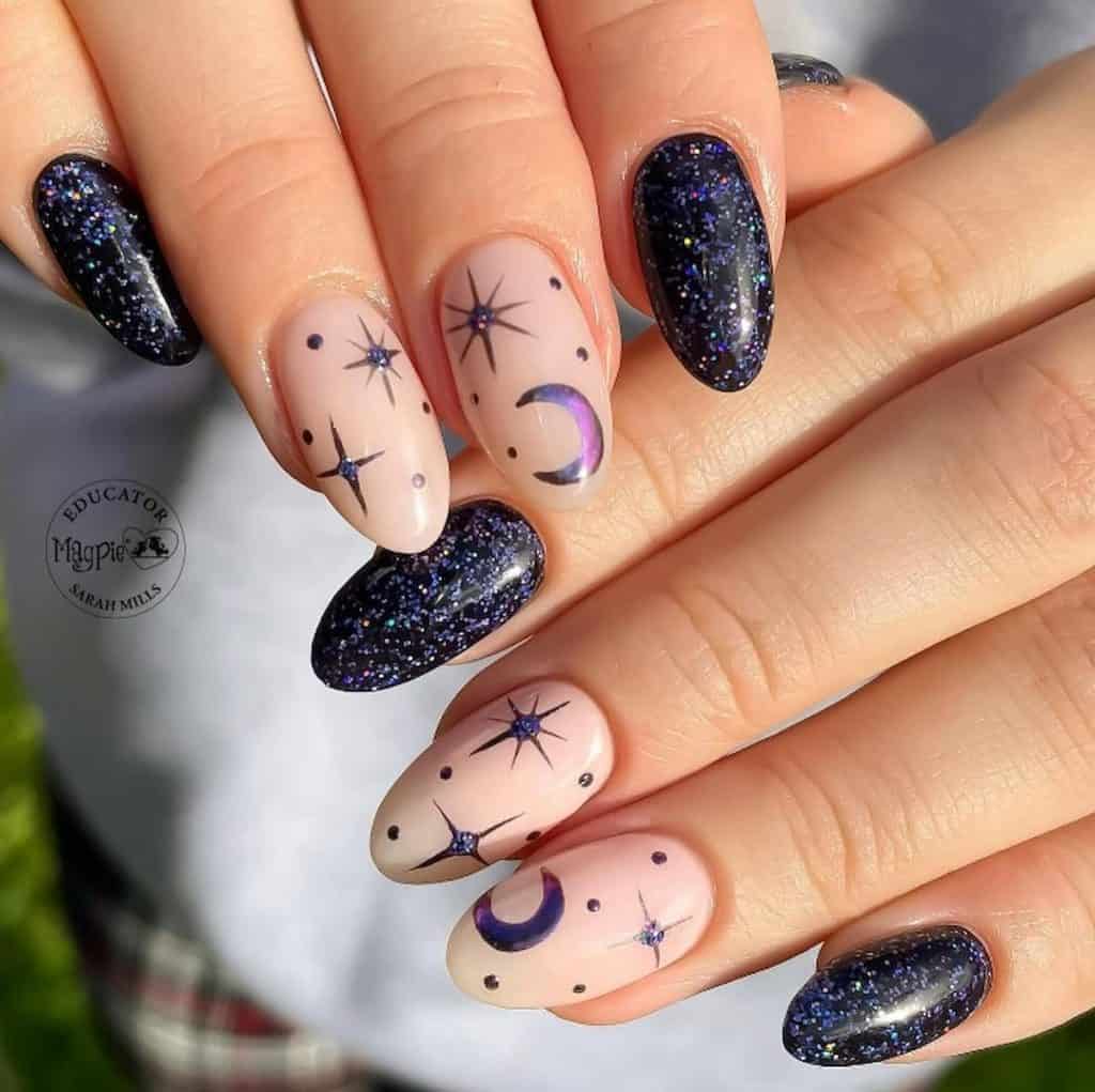 A closeup of a woman's hands with a pale pink and black nail polish that has moon, star stickers and blue glitter