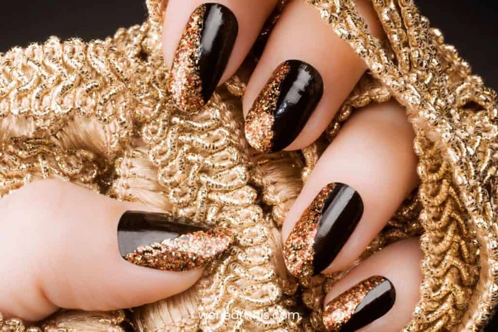A closeup of a woman's hands with a black nail polish base that has gold glitter