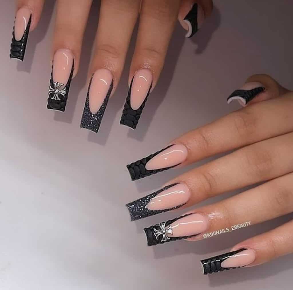 A woman's hands with a nude nail polish base and matte black and glitter nail tips that has silver cross on select nails