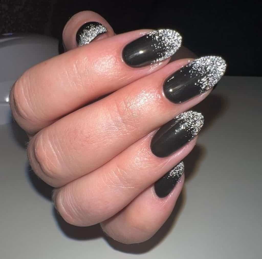 A closeup of a woman's hand with black nail polish base that has silver glitters on the nail tips