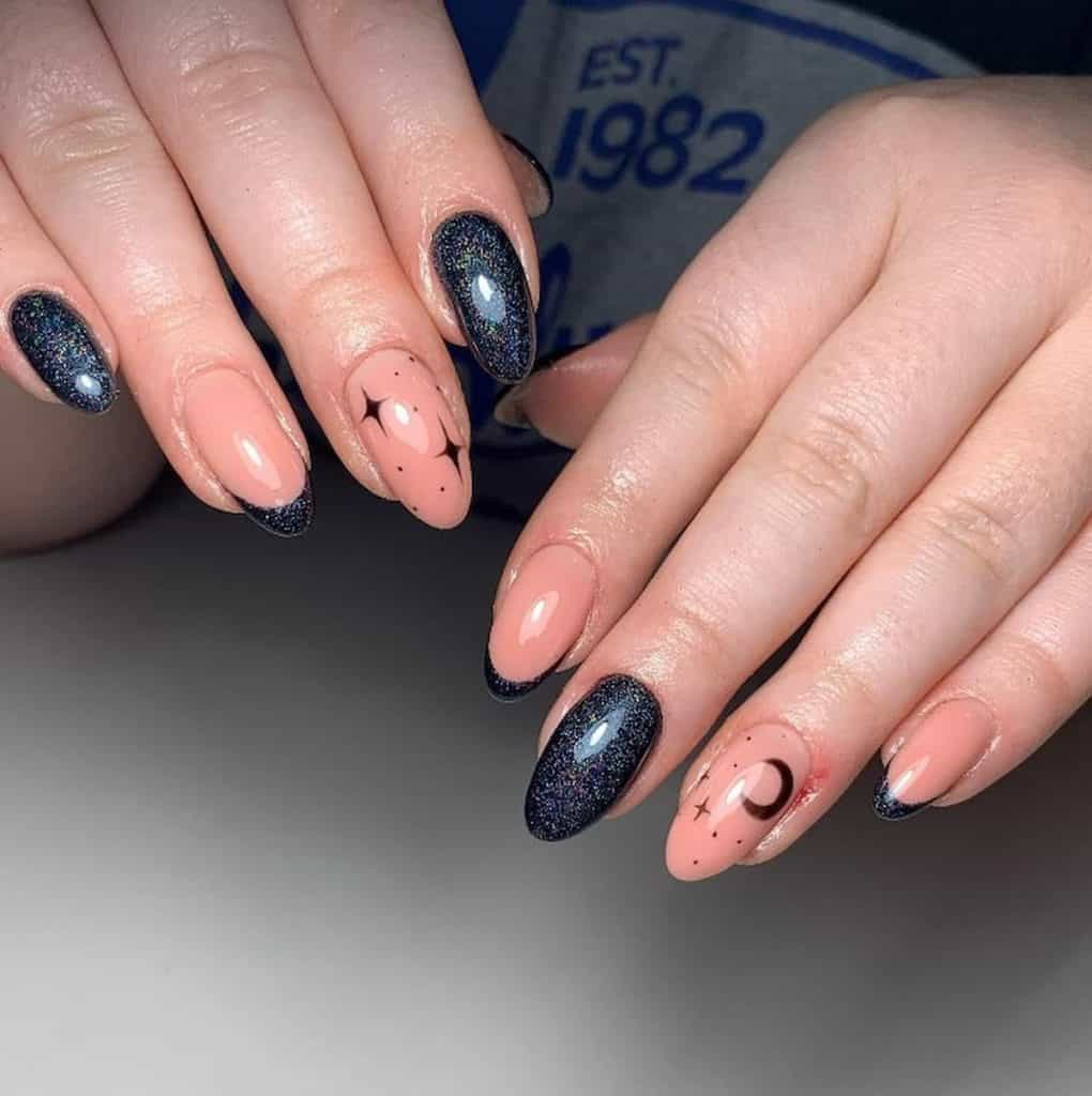 A closeup of a woman's hands with a combination of black and nude nail polish base that has deep blue glitter, stars and moon nail designs