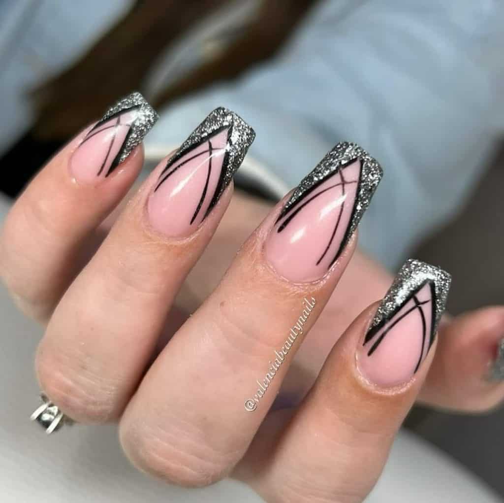 A closeup of a woman's hand with a nude nail polish base that has black pointed arch and silver glitter deep V-cut French tips