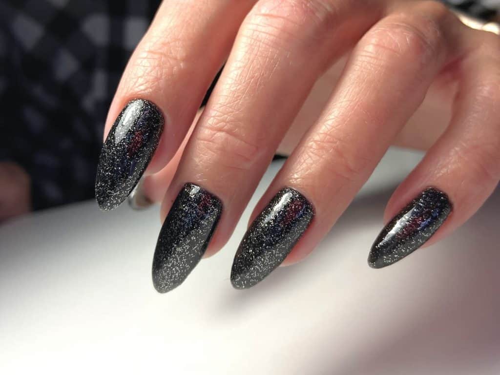 A woman's nails with black glitter on them.