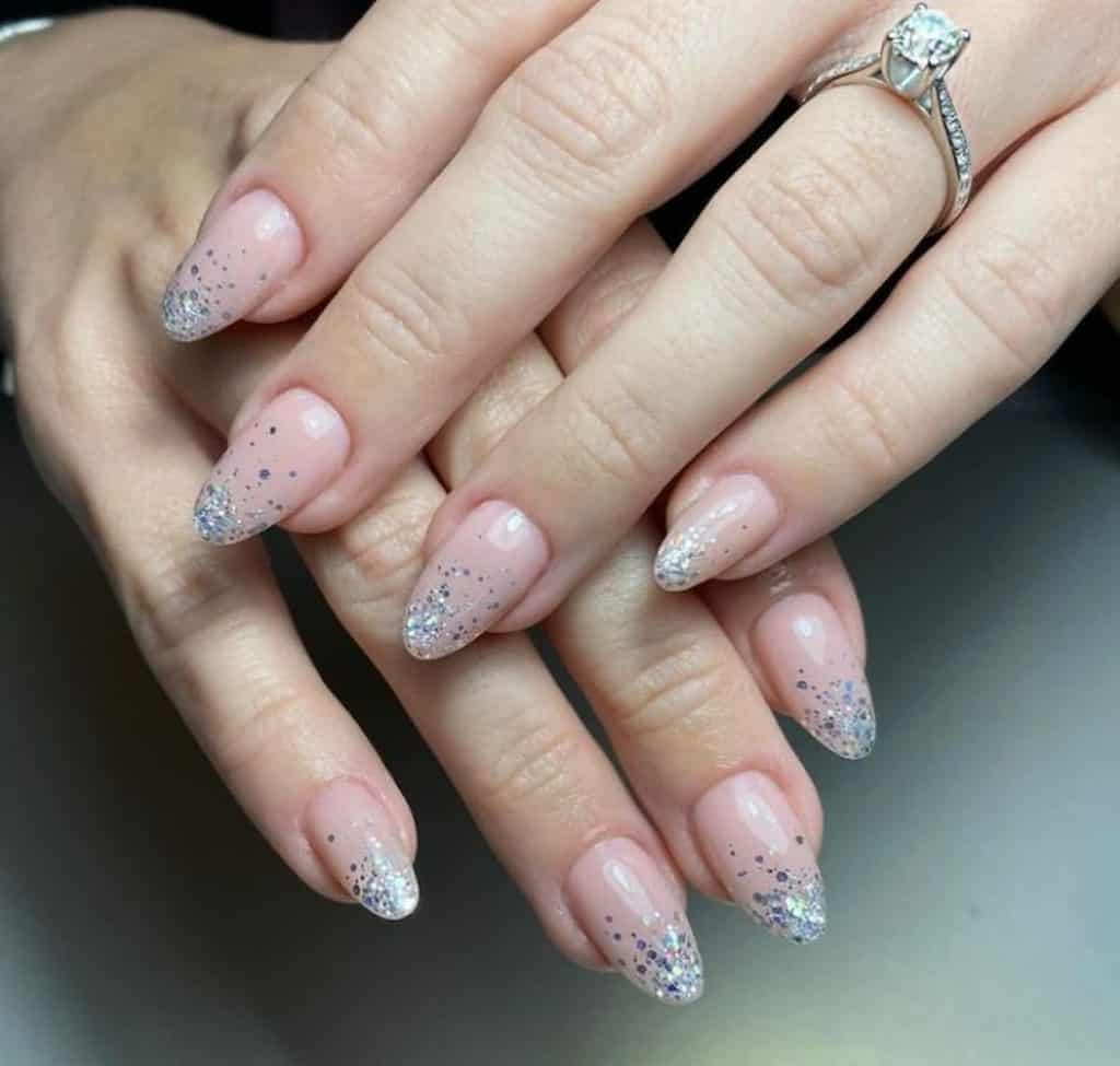 A closeup of a woman's hands with pale pink nail polish base that has white and pale blue glitters ombré nail designs