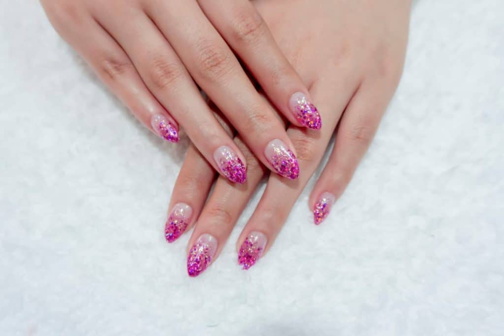 A woman's hands with neutral base that has rich hot pink glitter nail designs