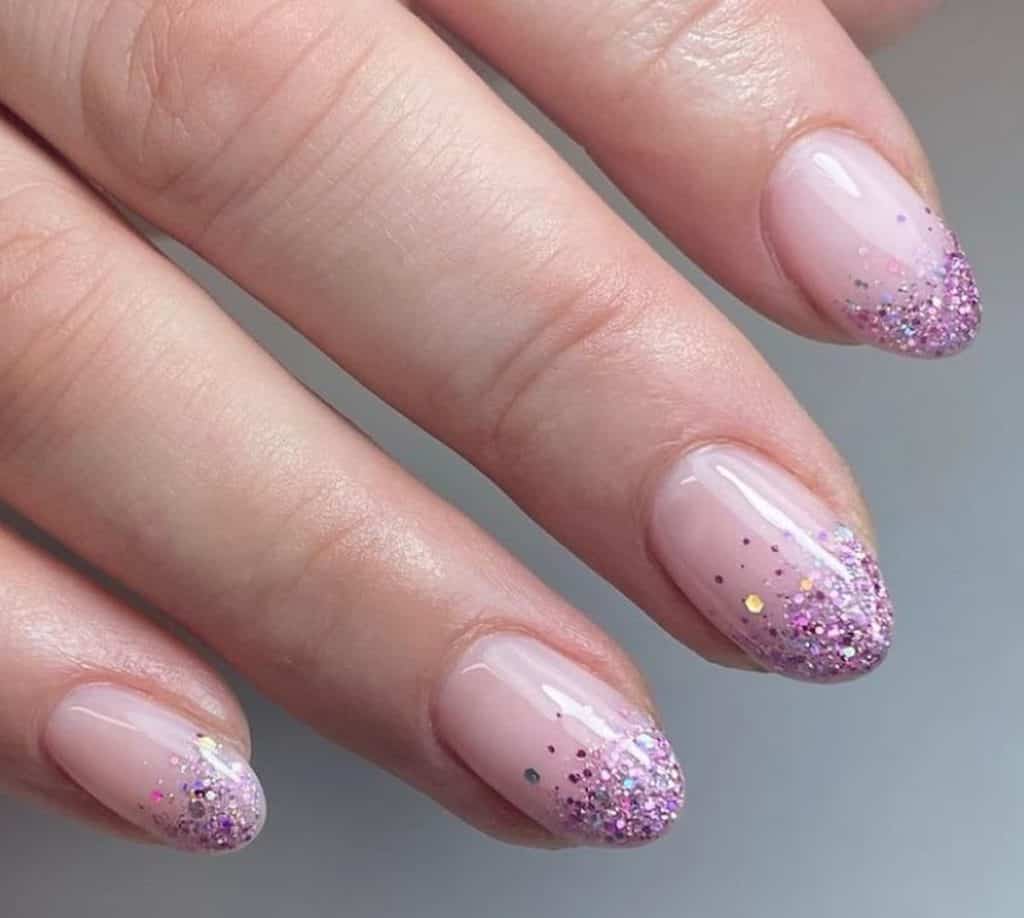 A closeup of a woman's hand with pale pink nail polish that has pink and purple hues of the glitter 