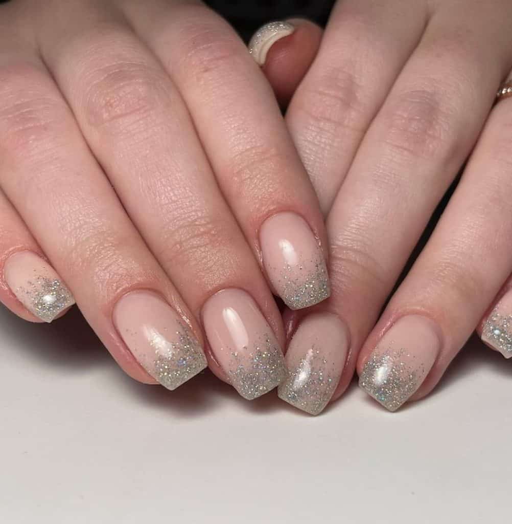 A closeup of a woman's hands with nude nail polish and silver glitter nail tips