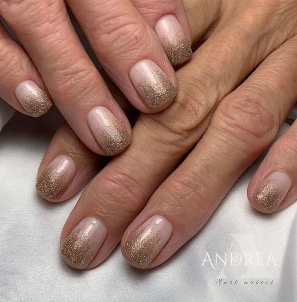 A closeup of a woman's hands with nude nail polish that has gold glitters on nail tips 