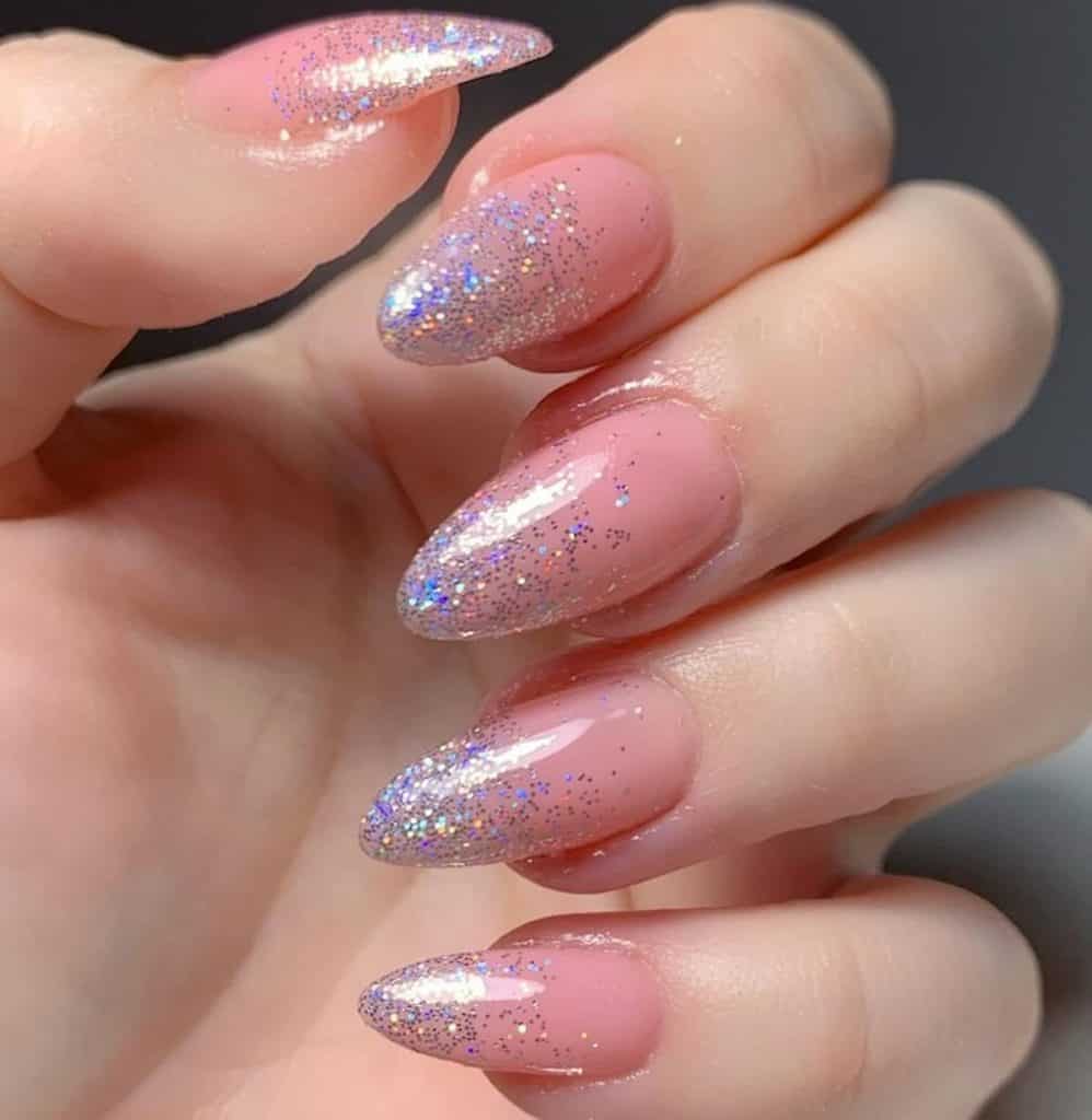 A closeup of a woman's hand with baby pink nail polish that has blue, silver, and gold flecks in holographic glitter tips