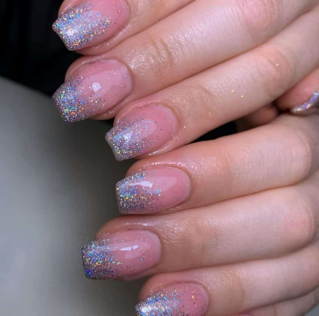 A closeup of a woman's hands with a pink nail polish that has silver glitters nail designs