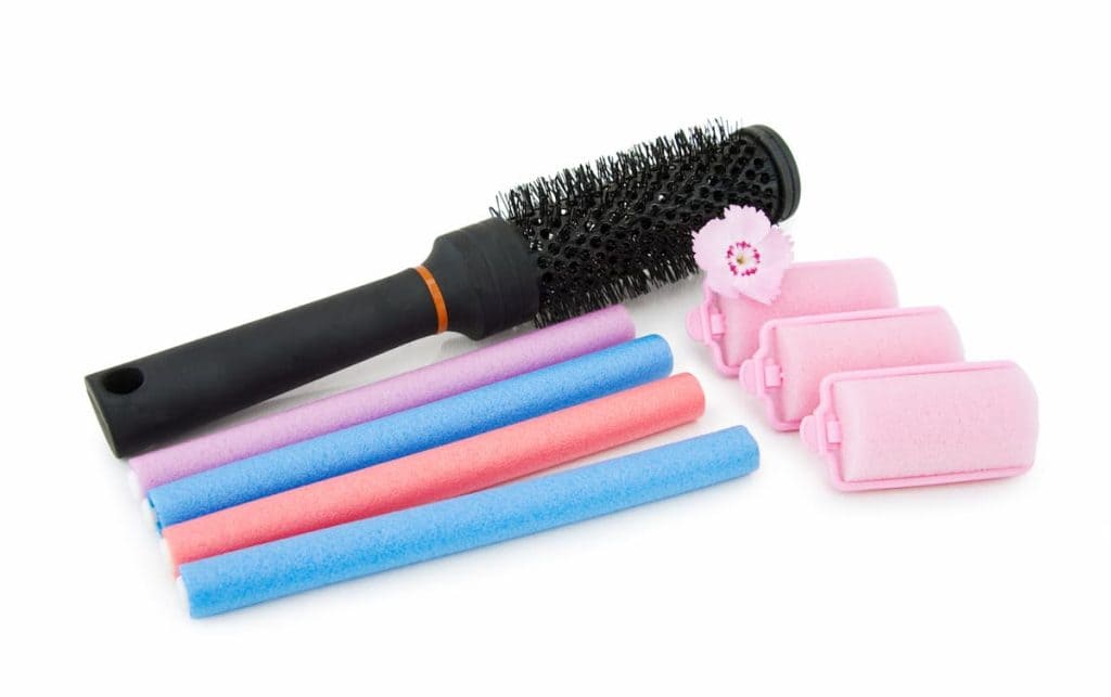 A hair brush with pink and several foam hair rollers on a white surface