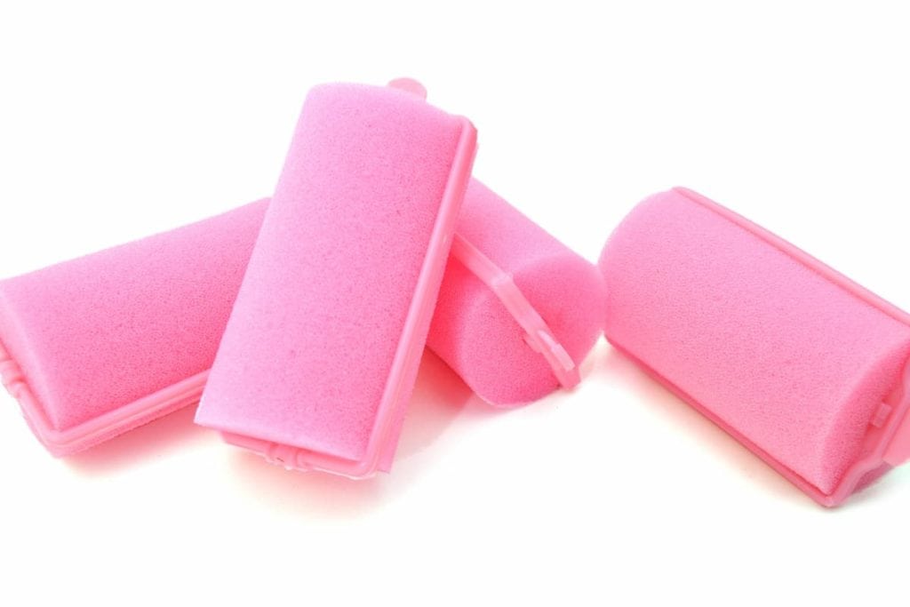 Four pink foam hair rollers on a white surface.