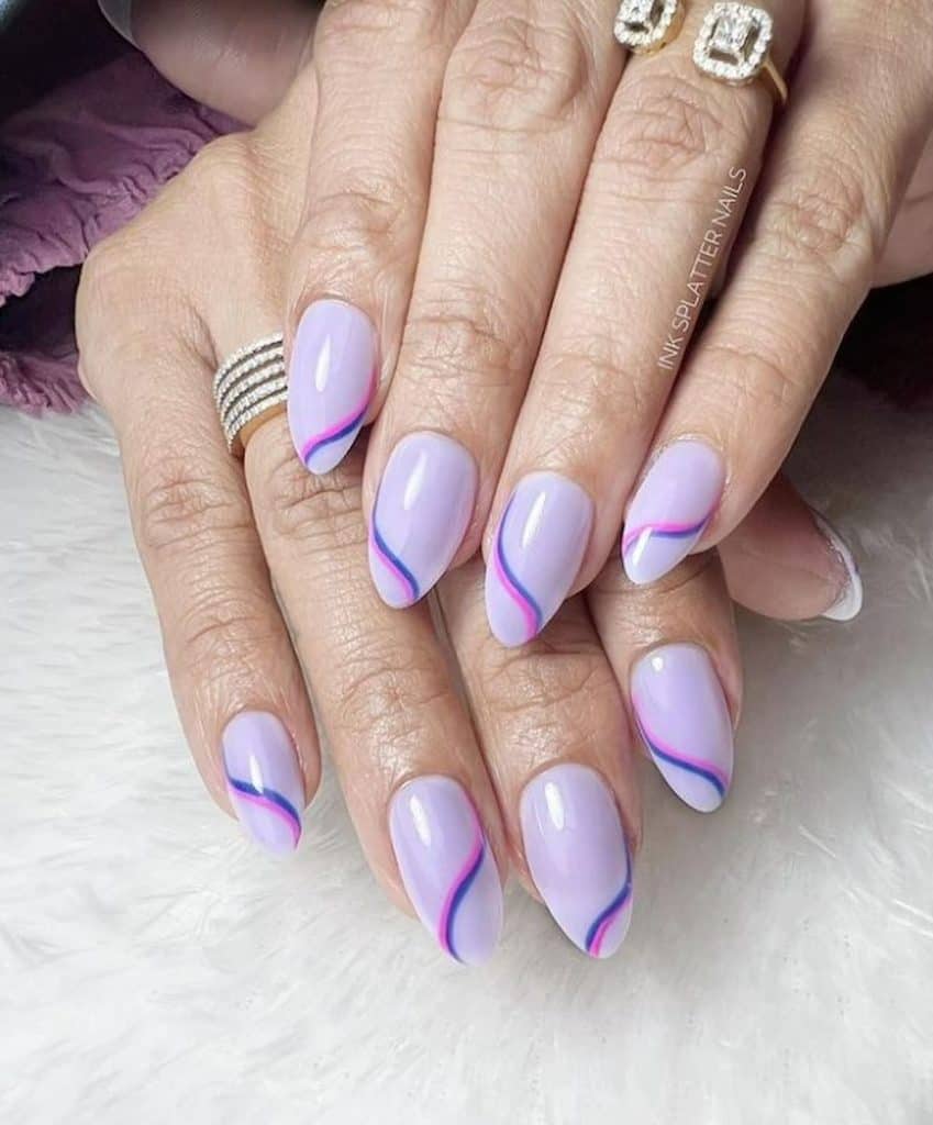 A woman's hands with a lavender colored nail polish. It has a combination of pink and blue curved stripes nail design