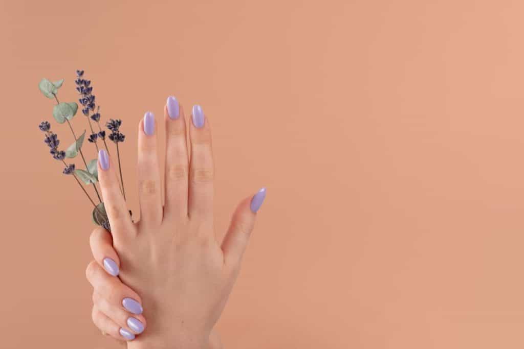 A woman's hands holding a flower with a lavender and lilac abstract nail design