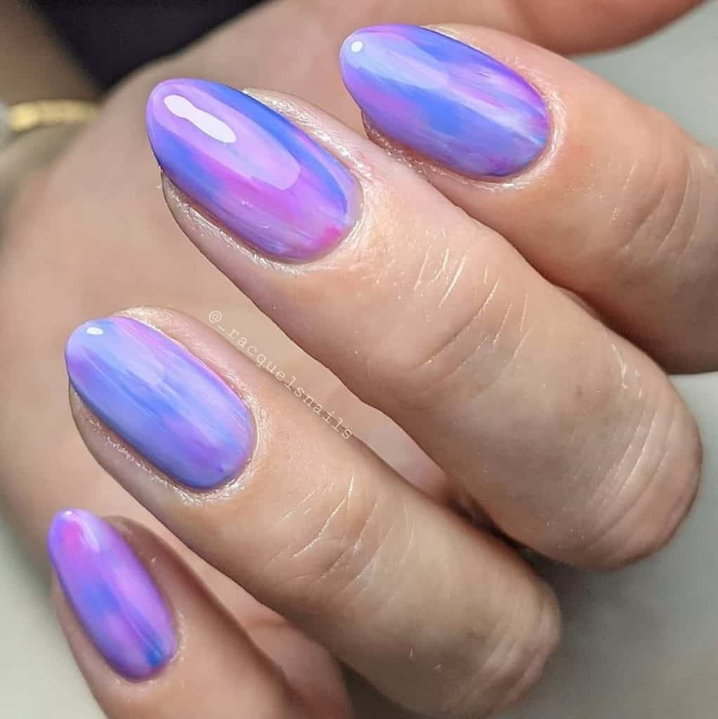 A closeup of a woman's hand having a combination of lavender, pastel blue, and pink nail polish 